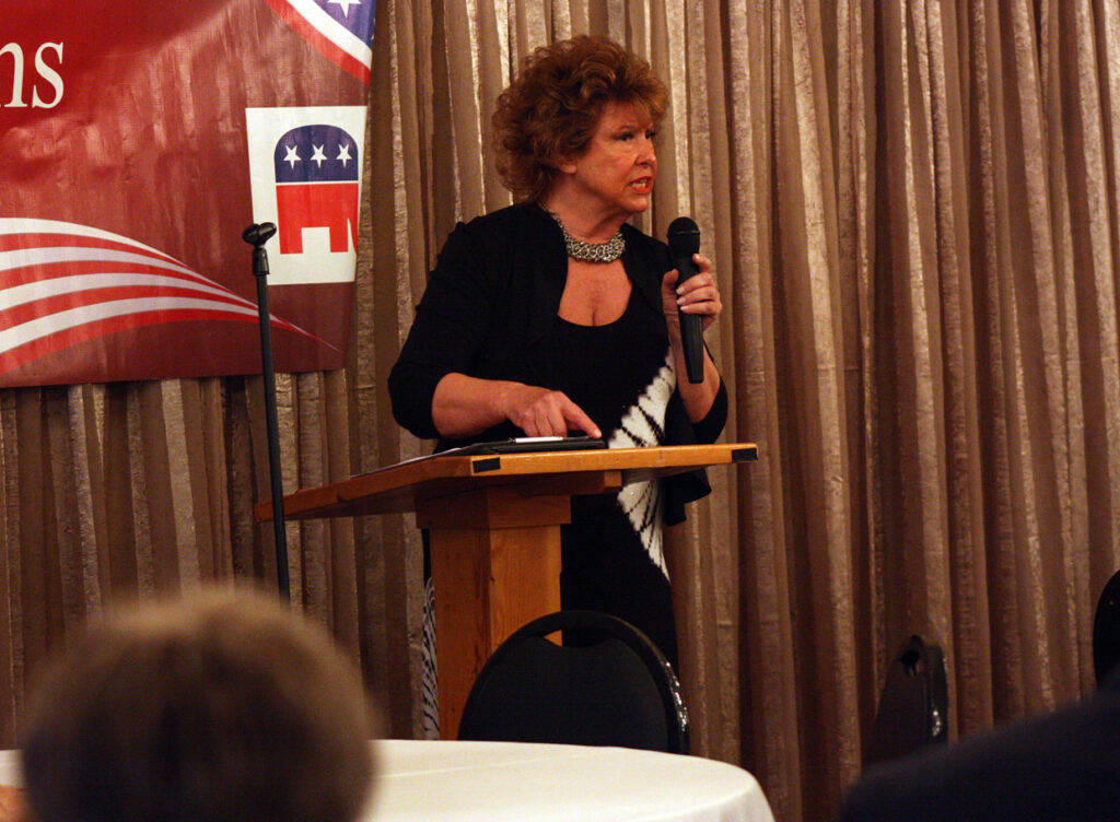 Woman standing at a podium speaking with GOP logo in background