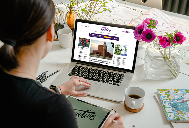 Woman looking at Richland Source website on her laptop with flowers and coffee on her table