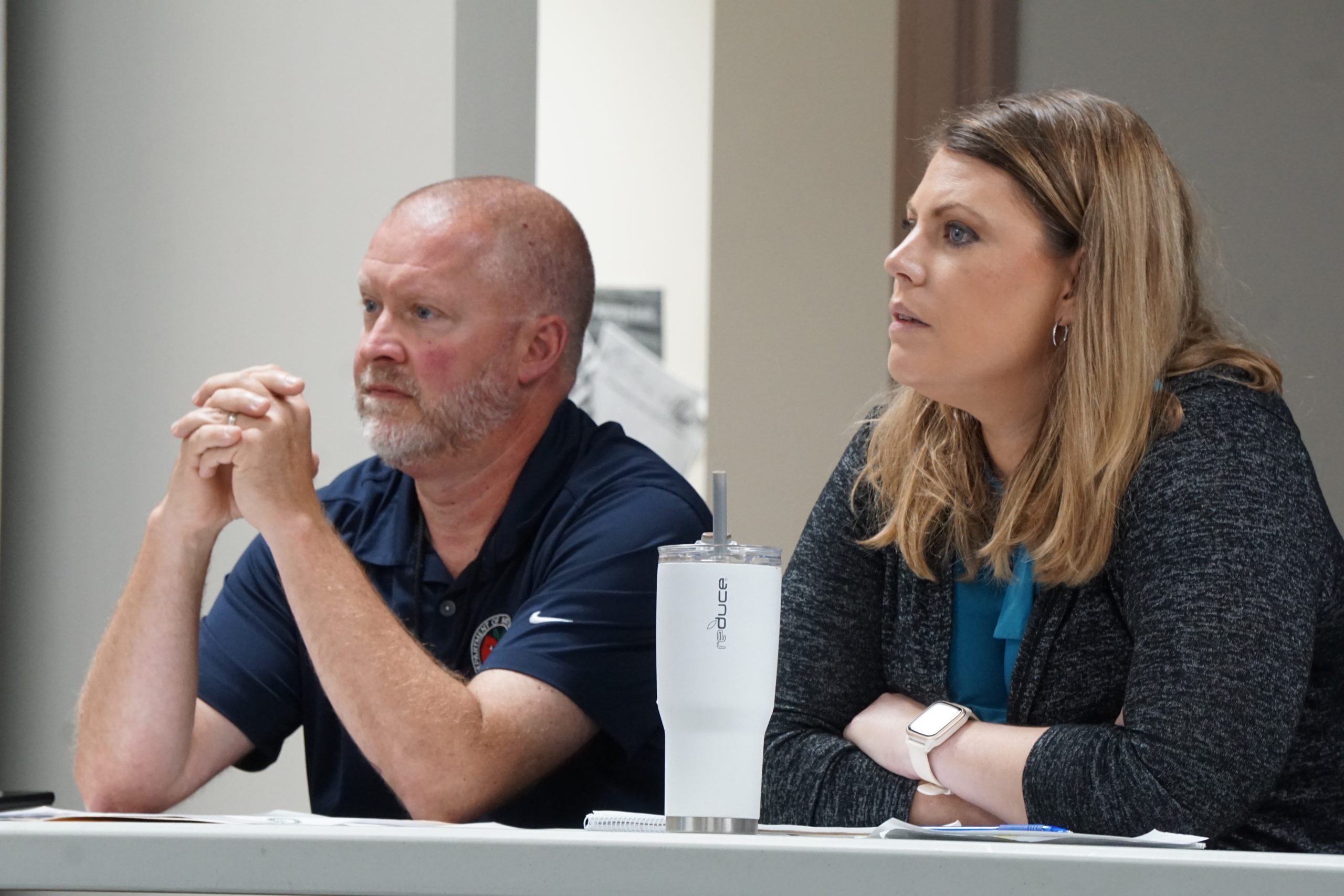 Man and woman sit at a table with a white cup on it.