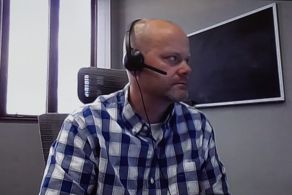 Man with headset sitting in front of computer camera.