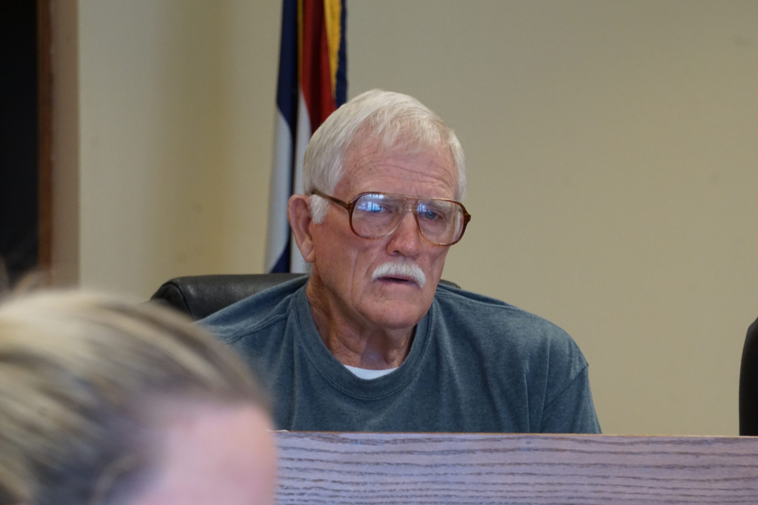 Man with white hair wearing a green sweatshirt.