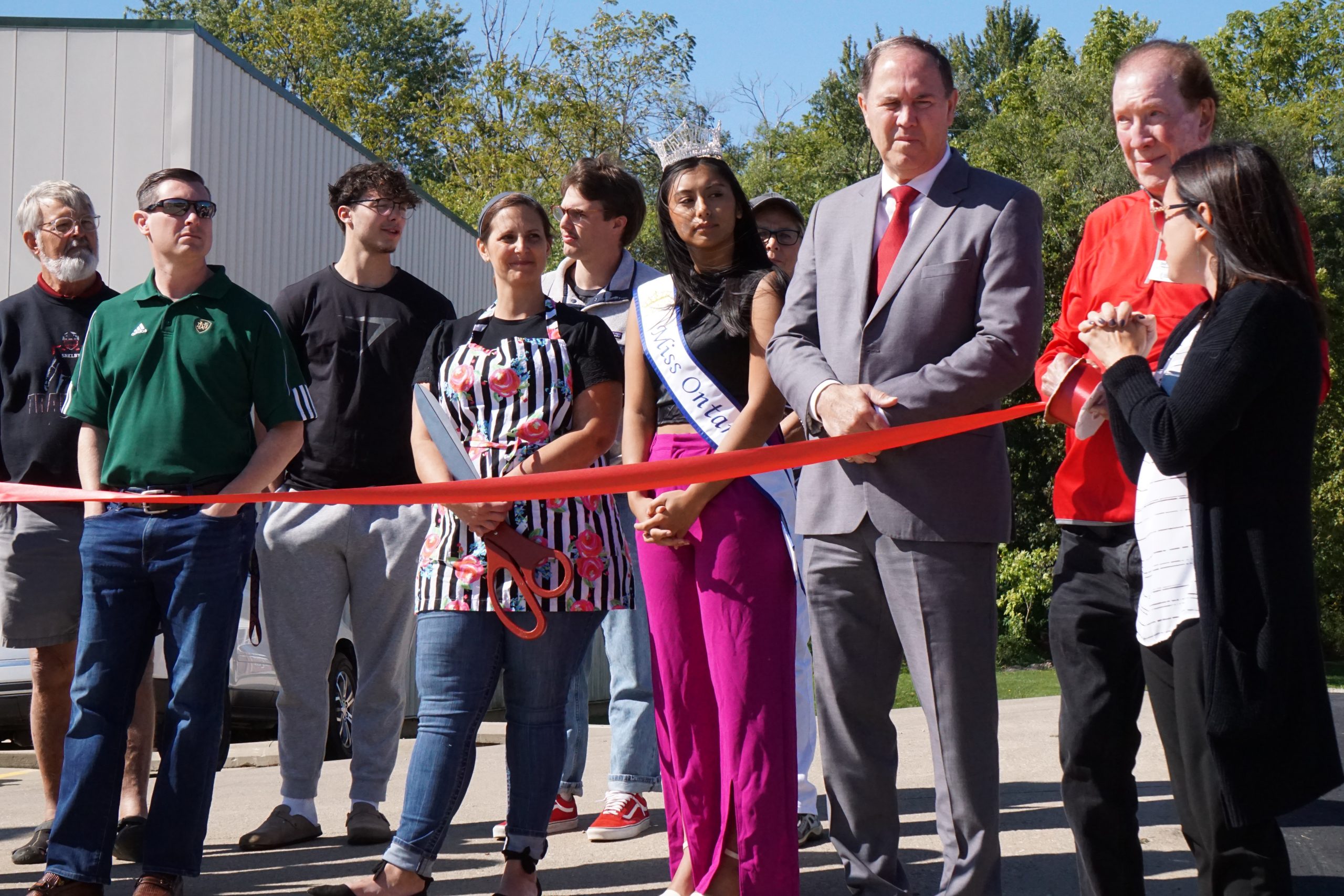 Row of people standing behind red ribbon.