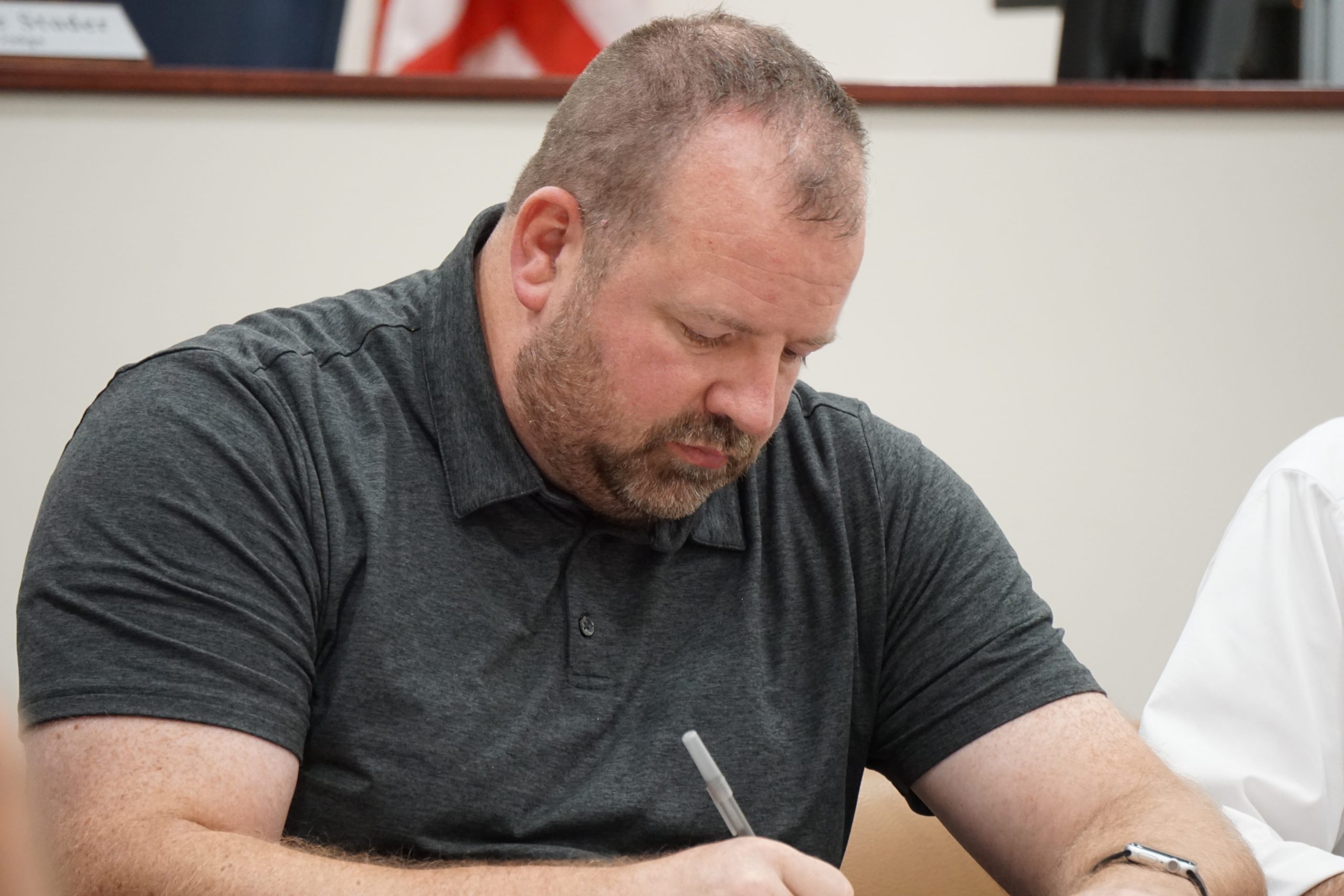 Man in gray polo writing with pen.
