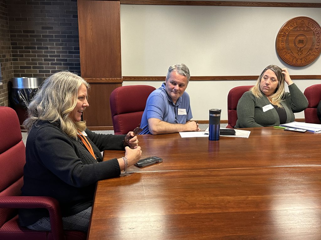 two middle aged women and a middle aged man sit at a table in a board room.