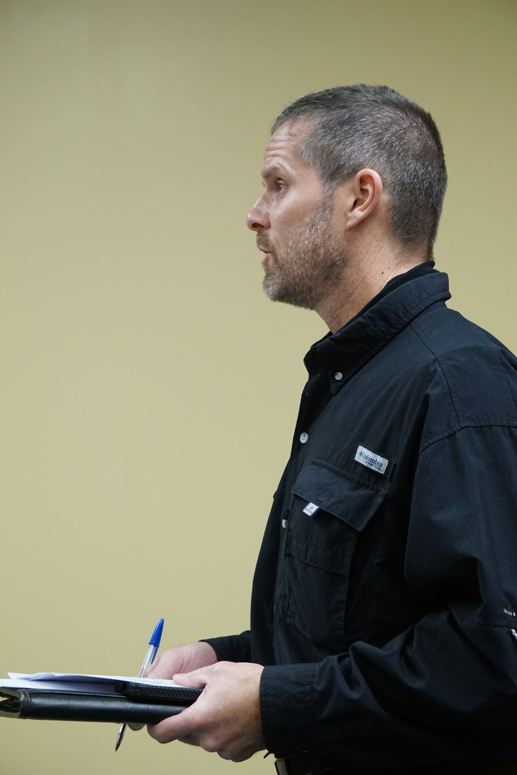 Man in black shirt holding pen and notebook.