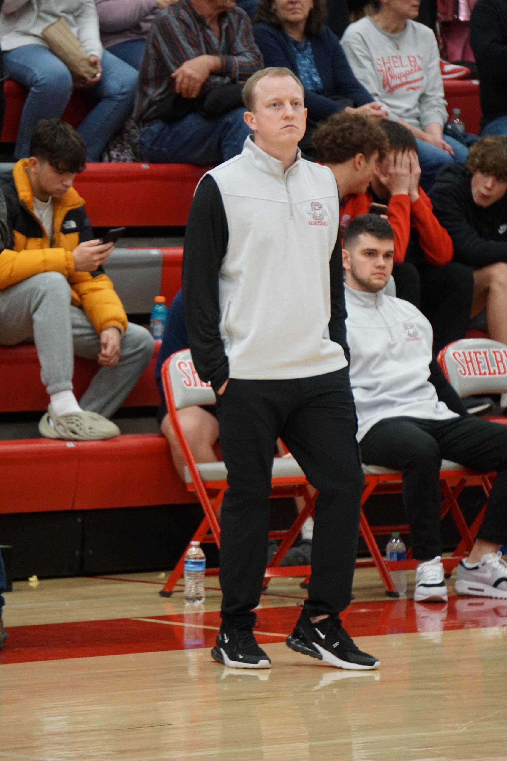 Man in gray vest and black pants standing on basketball court.
