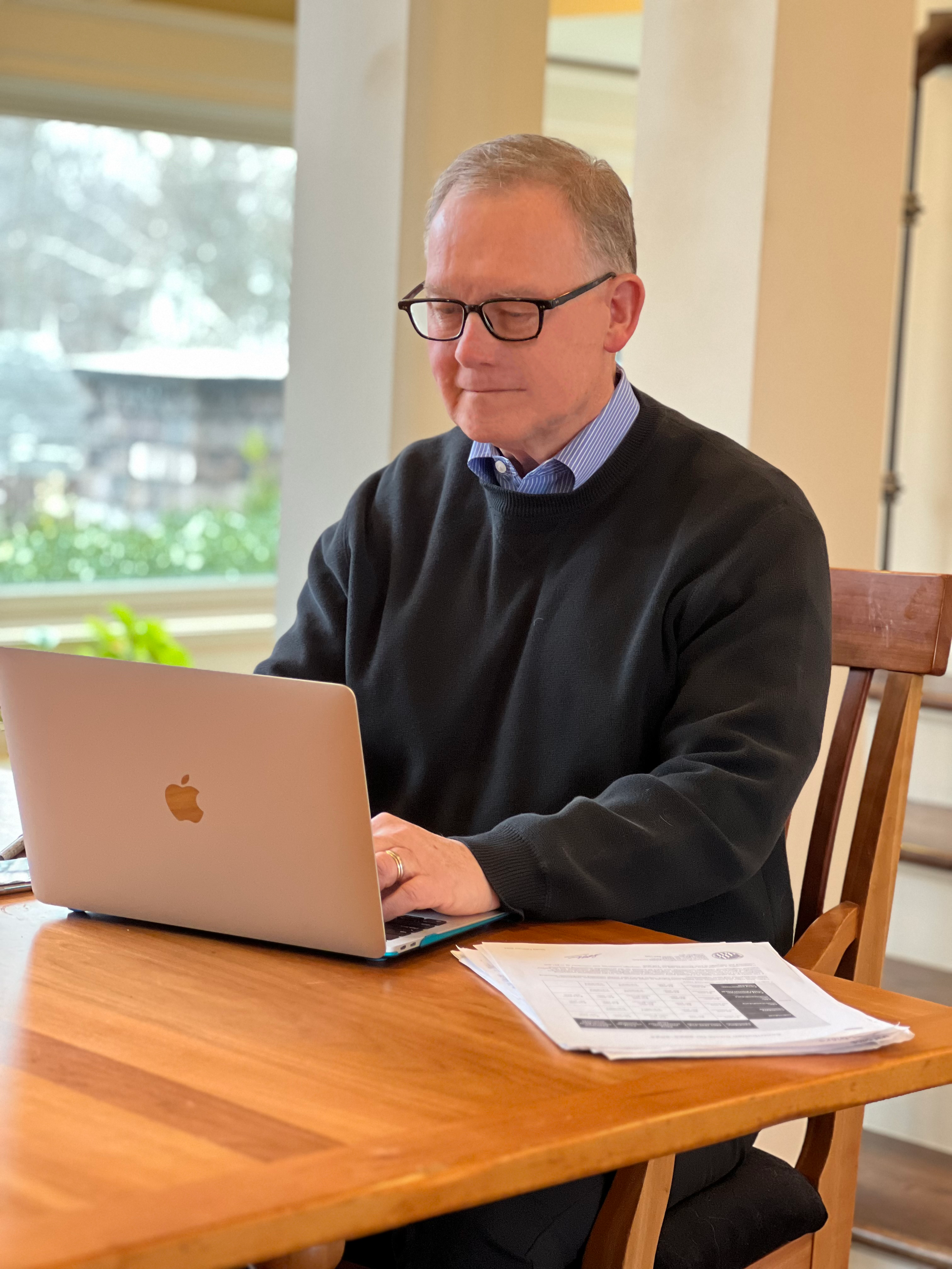Man in sweater sits at table typing on laptop