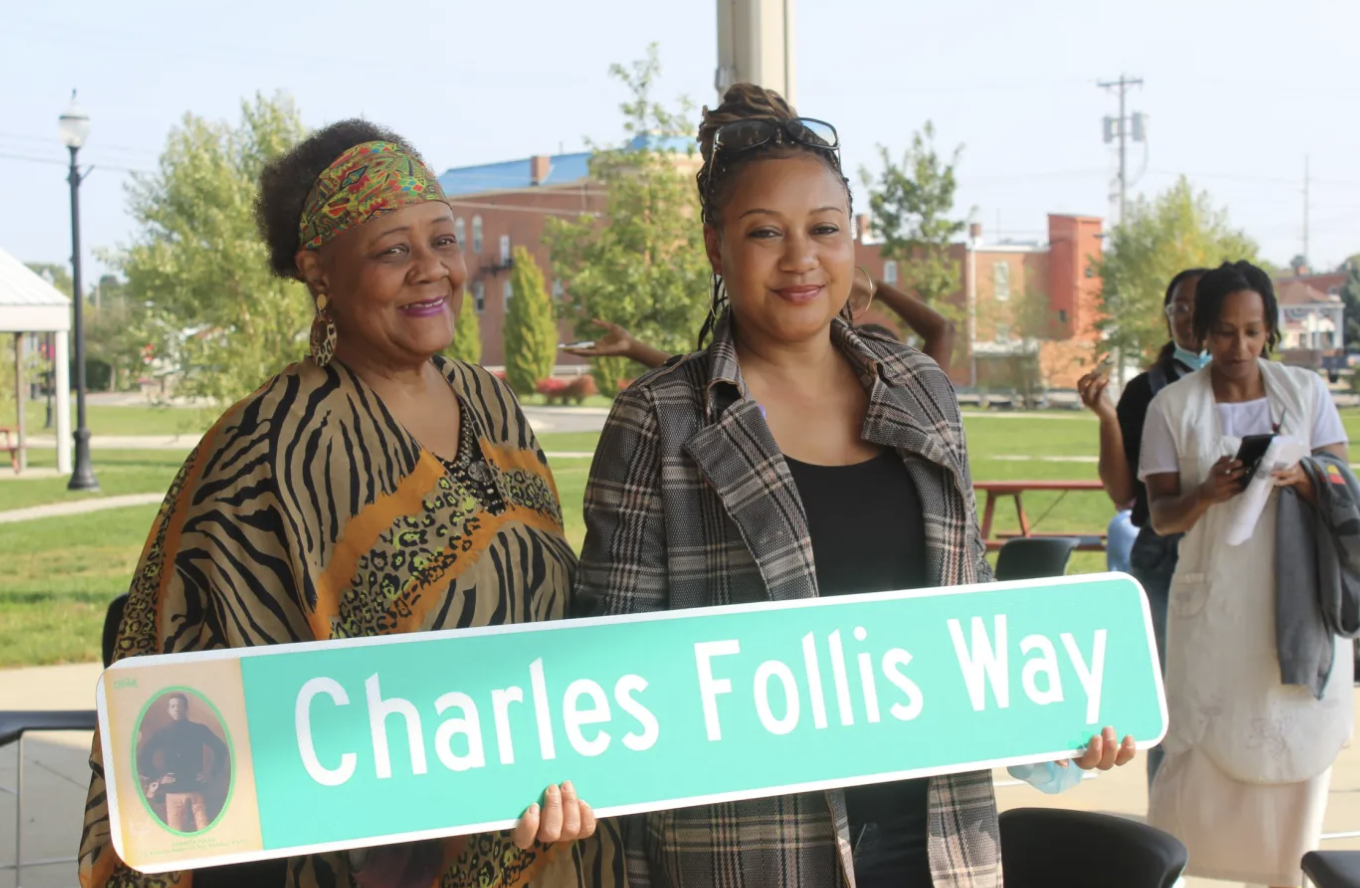 Two women holding a street sign in their hands.