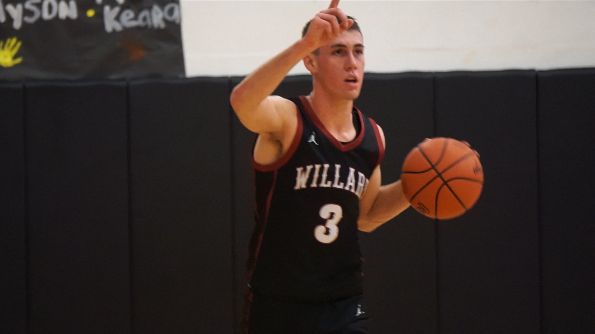 Basketball player dribbling ball, pointing with right hand