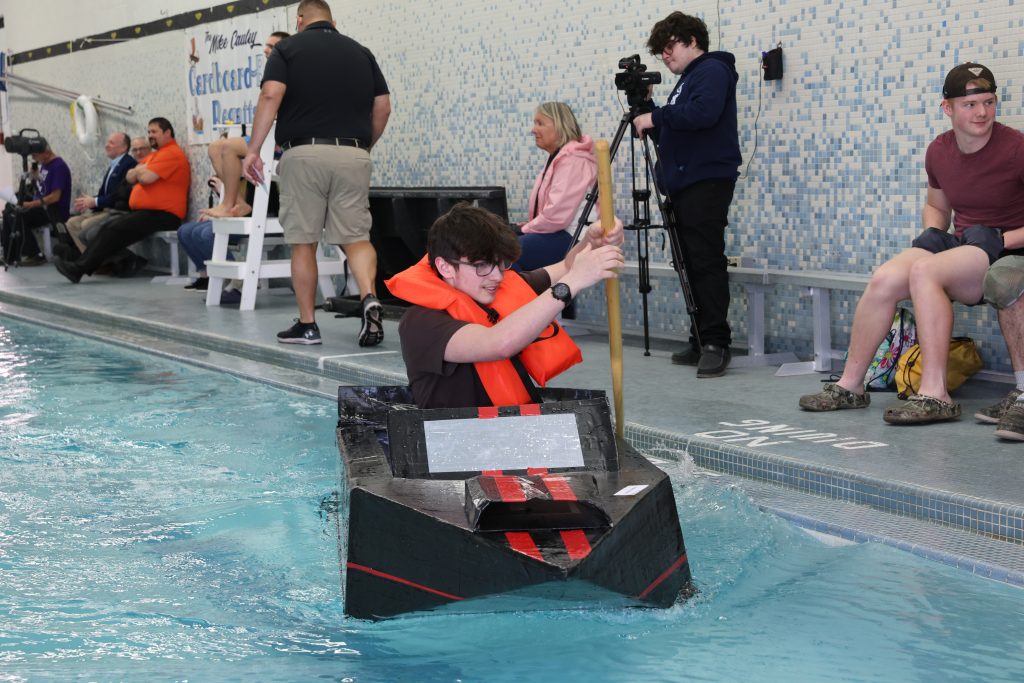 teenage boy races in Mike Cauley cardboard boat regatta at Colonel Crawford High School