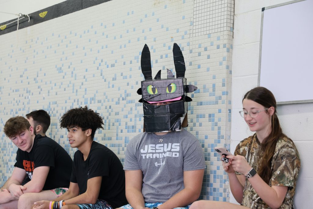 students watch cardboard boat regatta. one wears a how to train your dragon mask