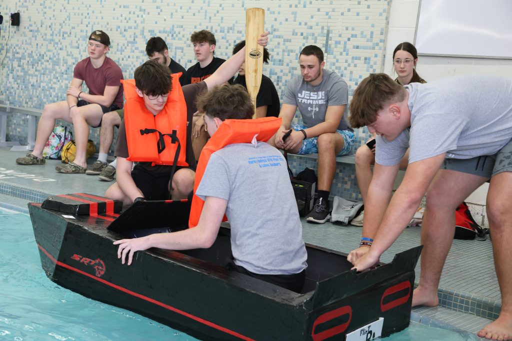 teenage boy races in Mike Cauley cardboard boat regatta at Colonel Crawford High School